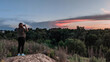 © Владимир Трубачёв - Person taking photo of colorful sunset landscape with smartphone from hilltop. Nature scenery, evening sky, clouds, forest, outdoor travel and mobile photography concept.