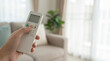 © Anastasiya - Hand uses remote control for aircon. Remote control sets cool fan in bright living room, home comfort for summer heatwave, energy saving, smart home lifestyle, clean interior with copy space