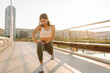 © maxbelchenko - Young woman in sportswear stretches on city bridge in sun. An athletic woman enjoys morning workout outdoors. Concept: sports, recreation, active lifestyle.