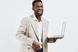© SHOTPRIME STUDIO - Smiling man wearing beige blazer and white shirt holding open laptop computer in hand, looking friendly, confident, and professional isolated on plain white background, studio portrait with modern