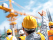 © Kowit - Construction workers communicate on-site, wearing safety helmets and vests, with a crane in the background.