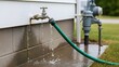 © Trendy_Desing - Green garden hose leaking water from outdoor silver spigot near gray water pump