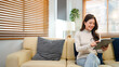 © Stella 16 - Happy young woman sitting on sofa in modern white living room, using Tablet computer to view content surrounded by bright natural light. Beautifull people and modern technology concept image.