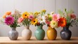 © Amy - five ceramic vases filled with vibrant mixed flowers arranged on a wooden surface against a light wall background
