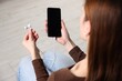 © New Africa - Woman holding smartphone with earphones indoors, closeup