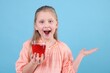 © New Africa - Little girl with glass of pomegranate juice showing something on light blue background. Space for text