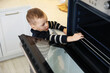 © New Africa - Child safety at home. Little boy taking rack out of oven in kitchen