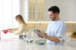 © New Africa - Man wiping plate while woman cleaning faucet of kitchen sink indoors, selective focus