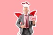© Pixel-Shot - Senior man dressed as Cupid holding paper with lipstick kiss marks on pink background. Valentine's Day celebration