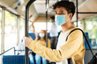 © Prostock-studio - Travel Safely On Public Transport. Portrait of young asian man in protective face mask looking through train window. Male passenger with backpack riding standing inside autobus, holding handle