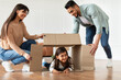 © Prostock-studio - Fooling Around. Happy loving family of three people playing together, celebrating relocation day, cute little daughter lying on floor inside cardboard box, imitating house, spending time together