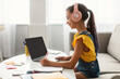 © Prostock-studio - Side view profile portrait of girl in pink headset doing homework, sitting on couch at table using laptop with empty screen, writing essay or making test, taking notes in textbook, free copy space