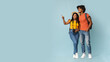 © Prostock-studio - Happy millennial black couple tourists with backpacks and camera embracing and looking at copy space on blue studio background, choosing destination to travel, panorama. Travelling concept