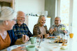 © Davor - Senior friends laughing over lunch at home dining table