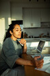 © Marko Geber - Young woman paying bills on laptop at home kitchen
