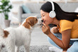 © Prostock-studio - Loving millennial asian woman cuddling with her pet at home, smiling young korean lady sitting on floor in living room with wireless headset, listening to music and petting adorable dog, closeup