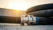 © Hazeel - Industrial black hose with silver metal connector on concrete ground at sunset - Ai Generated