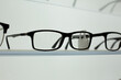 © malazoniia - Clear prescription glasses with black frames on glass shelf next to other glasses. Suitable glasses for person with vision problems. Glasses for improving vision on shelf. Corrective vision
