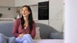 © fizkes - Laughing middle-aged 40s woman homeowner in casual clothes sits on comfortable sofa in cozy studio apartment, fashionable kitchen in background, copy space view. Relaxation at home, carefree pastime