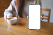 © Farknot Architect - Mockup image of a woman holding and showing a mobile phone with blank white screen while drinking cafe