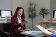 © Tj - Asian businesswoman discussing company reports and financial data with a colleague during a professional meeting in a modern office environment, demonstrating collaboration and mentorship