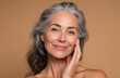 © AndiAzis - Mature woman in her fifties with elegant gray hair, radiant smile, and smooth skin, posing thoughtfully against a neutral background