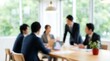 © CuteBee - A blurred, soft-focused scene captures several business professionals engaged in an interactive meeting around a wooden conference table in a bright, modern office environment.