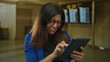 © Krakenimages.com - Woman in blue blazer and glasses holds tablet and pumps fist in crowded airport terminal while smiling broadly with excitement; victory.
