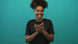 © Krakenimages.com - Young african american woman clapping hands and smiling in teal studio, wearing black shirt, playful pose; joy celebration.