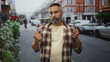 © Krakenimages.com - Man holding two metal faucets with bare hands on city street, gripping the taps and frowning beside parked cars and buildings; frustration.