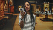 © Krakenimages.com - Black woman holding a smartphone, hand and face visible, smiling while looking at the screen inside a museum; curiosity.