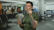 © Krakenimages.com - Young man holding us dollars confidently pointing in an airport terminal, symbolizing wealth and travel.