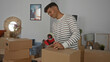 © Krakenimages.com - Young man packing boxes in a living room of a new home, preparing for a move with cardboard boxes and tape.
