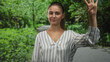 © Krakenimages.com - Woman raises hand with palm visible on a forest path, striped blouse and relaxed posture; serenity.