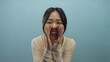 © Krakenimages.com - Young chinese woman shouting enthusiastically against an isolated blue background, capturing an energetic and cheerful moment.