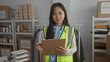 © Krakenimages.com - Woman in reflective vest taking notes at indoor charity center surrounded by donations depicting volunteer work and organization of supplies.