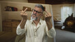 © Krakenimages.com - Man showing middle finger with both hands, grimacing and wearing glasses and a beige shirt in a living room building; defiance.
