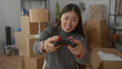 © Krakenimages.com - Woman playing video games in new home surrounded by moving boxes, capturing joyful unpacking moment in apartment's cozy interior.