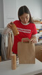 © Krakenimages.com - Woman packing donations in charity center wearing red volunteer shirt in indoor setting with canned goods and bags around her