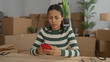 © Krakenimages.com - Woman smiling in new apartment surrounded by moving boxes using smartphone indoors with plants and lamp.