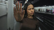© Krakenimages.com - Young woman at train station standing indoors with hand raised, expressing no or stop gesture, amidst the blurred railway setting, intent in her expression.
