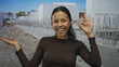 © Krakenimages.com - Young hispanic woman smiling at a construction site, making an 'ok' gesture, suggesting positivity and success in a dynamic outdoor environment.