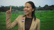 © Krakenimages.com - Woman in park smiles with finger raised wearing an i voted badge celebrates outdoors against green park backdrop suggesting civic pride and engagement in the united states.