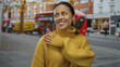 © Krakenimages.com - Hispanic woman in yellow sweater smiling on bustling city street with buses and trees in the background, capturing an urban autumn atmosphere.