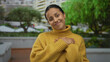 © Krakenimages.com - Young hispanic woman wearing yellow sweater warmly smiling outdoors in urban street setting surrounded by greenery and buildings, exuding happiness and contentment