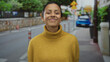 © Krakenimages.com - Woman wearing yellow sweater smiles warmly on a quiet street, with blurred city background and green foliage, embodying casual urban outdoor ambiance and hispanic heritage.