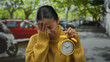 © Krakenimages.com - Woman outdoors holding alarm expressing frustration on street in urban setting, surrounded by cars, trees, and wearing a yellow sweater, portraying urgency and time management issues.