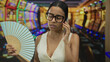 © Krakenimages.com - Woman talking on phone holding fan in stylish casino surrounded by colorful slot machines, portraying relaxation and urban lifestyle indoors.