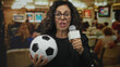 © Krakenimages.com - Woman holding microphone and soccer ball in art gallery setting, middle-aged hispanic reporter conveying sports news indoors.
