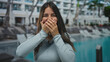© Krakenimages.com - Woman surprised at resort pool with hands covering mouth outdoors showcasing joyful reaction against a hotel backdrop